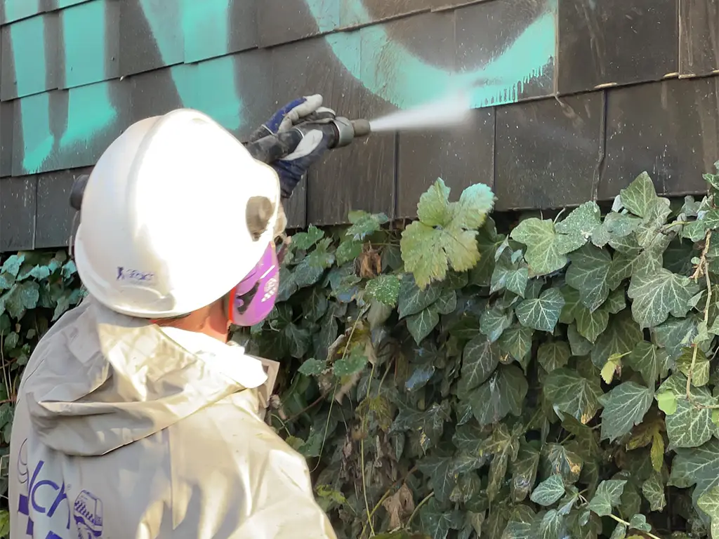 Arbeiter in Schutzkleider entfernt Graffiti mit Hochdruckreiniger